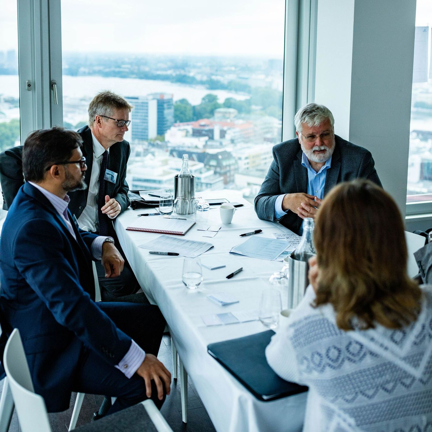 Business professionals having a discussion at a modern office conference table with city views through large windows.