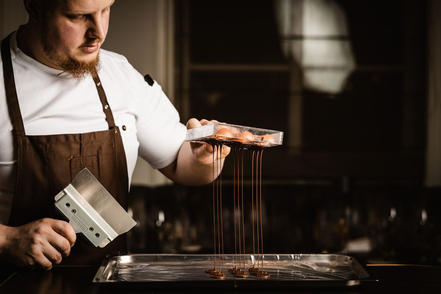 A barista carefully pours hot water over coffee grounds in a pour-over brewing setup in a dimly lit cafe setting.