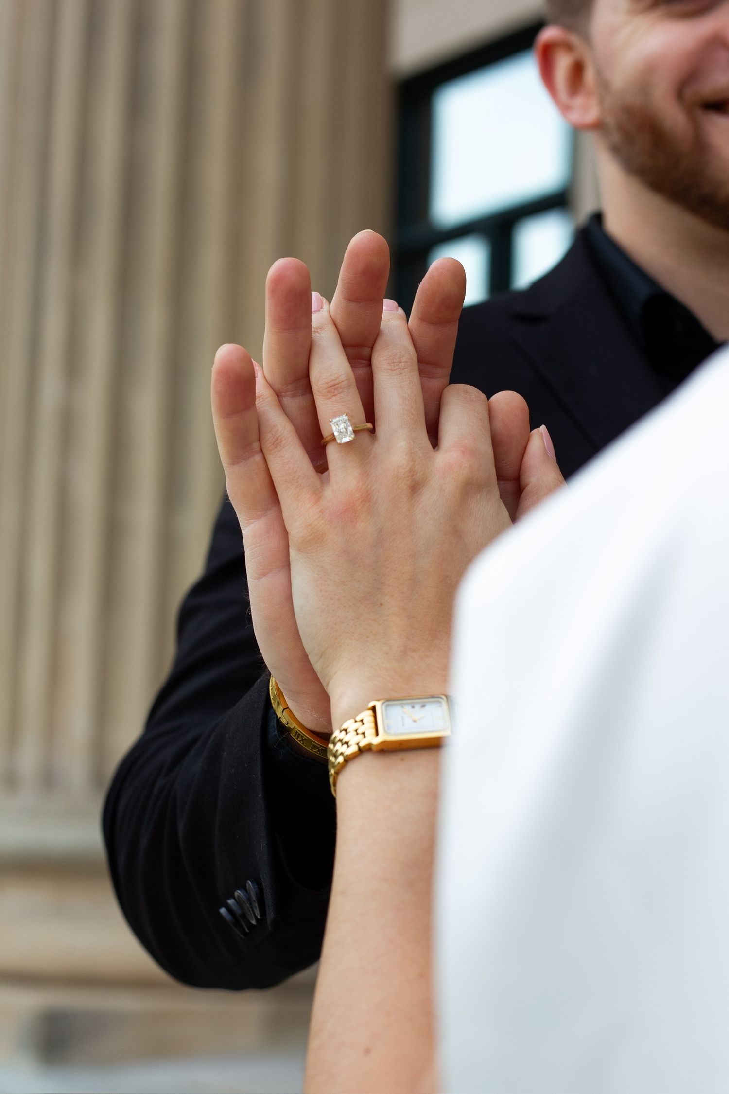 Couple holding hands showing diamond engagement ring and gold watch at wedding ceremony.
