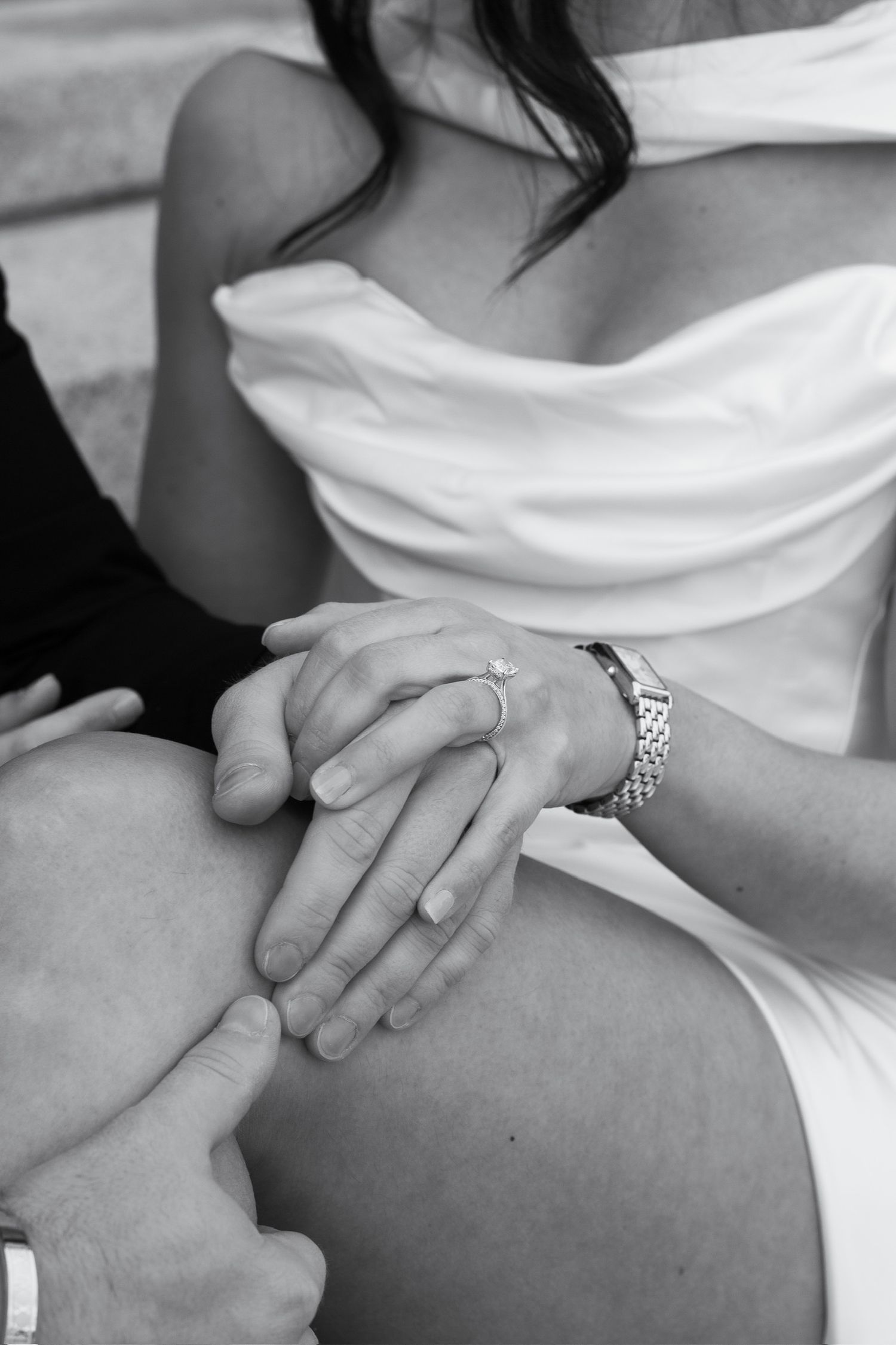 Black and white close-up of bride and groom holding hands, showing diamond engagement ring and bracelet on wedding day.