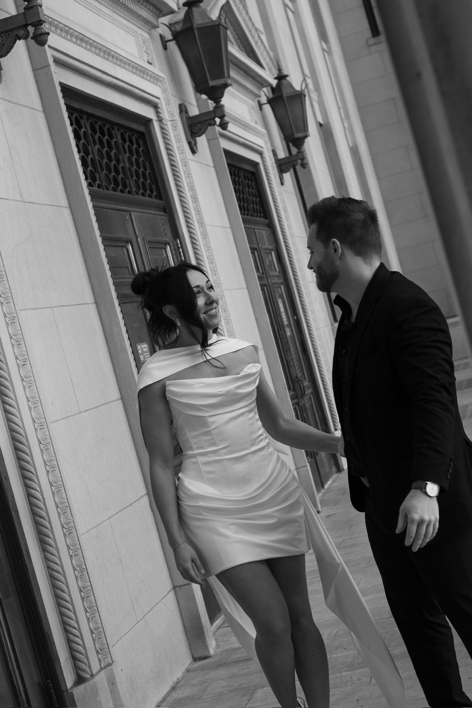 Black and white photo of a couple in wedding attire sharing a romantic moment against an ornate building.