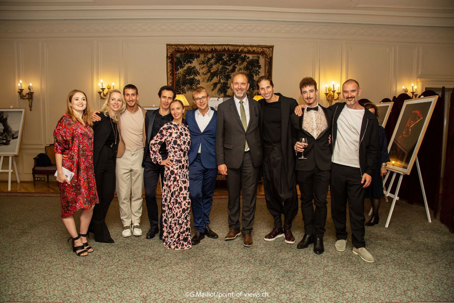 Group of elegantly dressed people posing together at a formal indoor event with artwork displayed in the background.