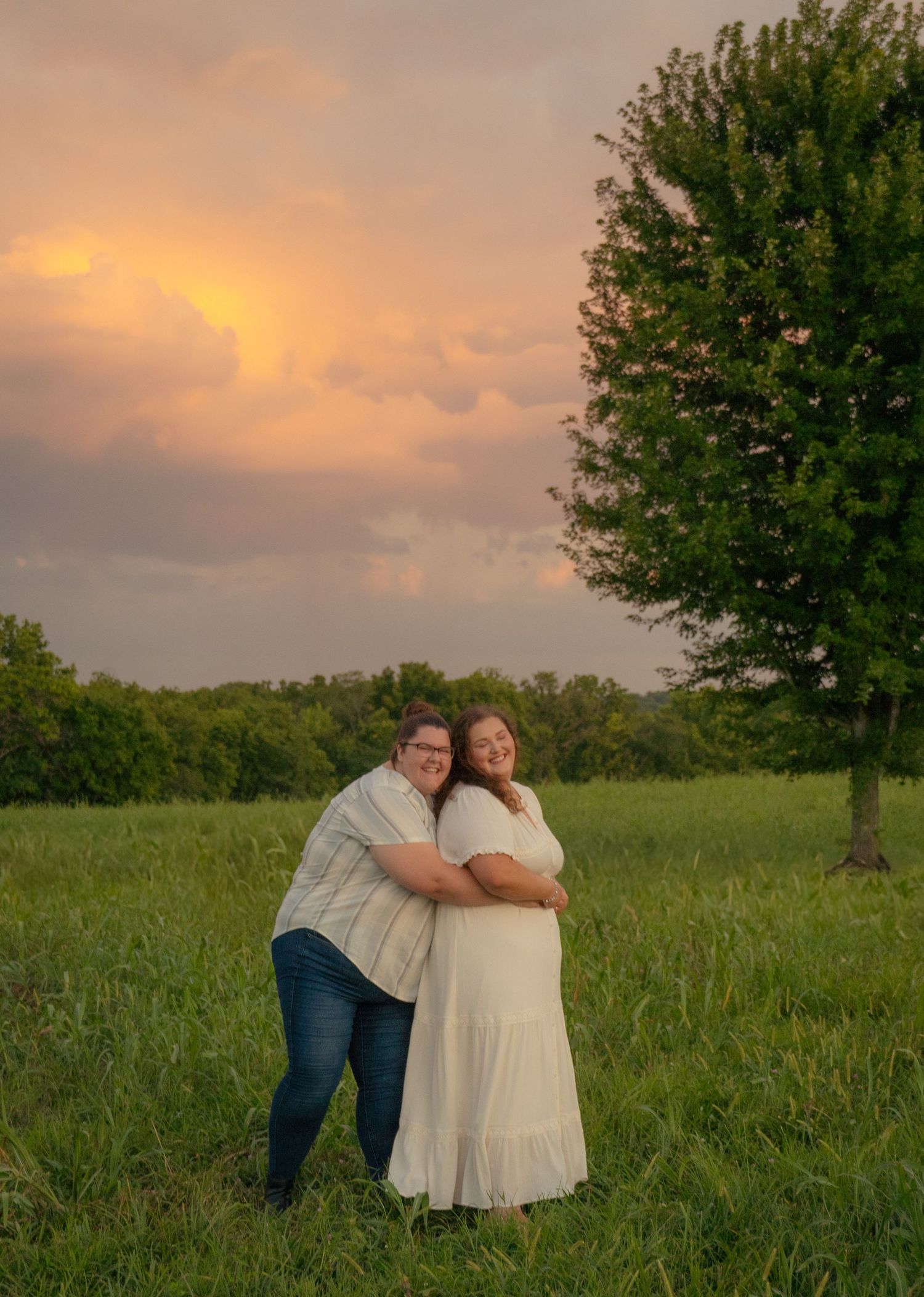 Romantic sunset photoshoot of couple embracing in a grassy field with trees.
