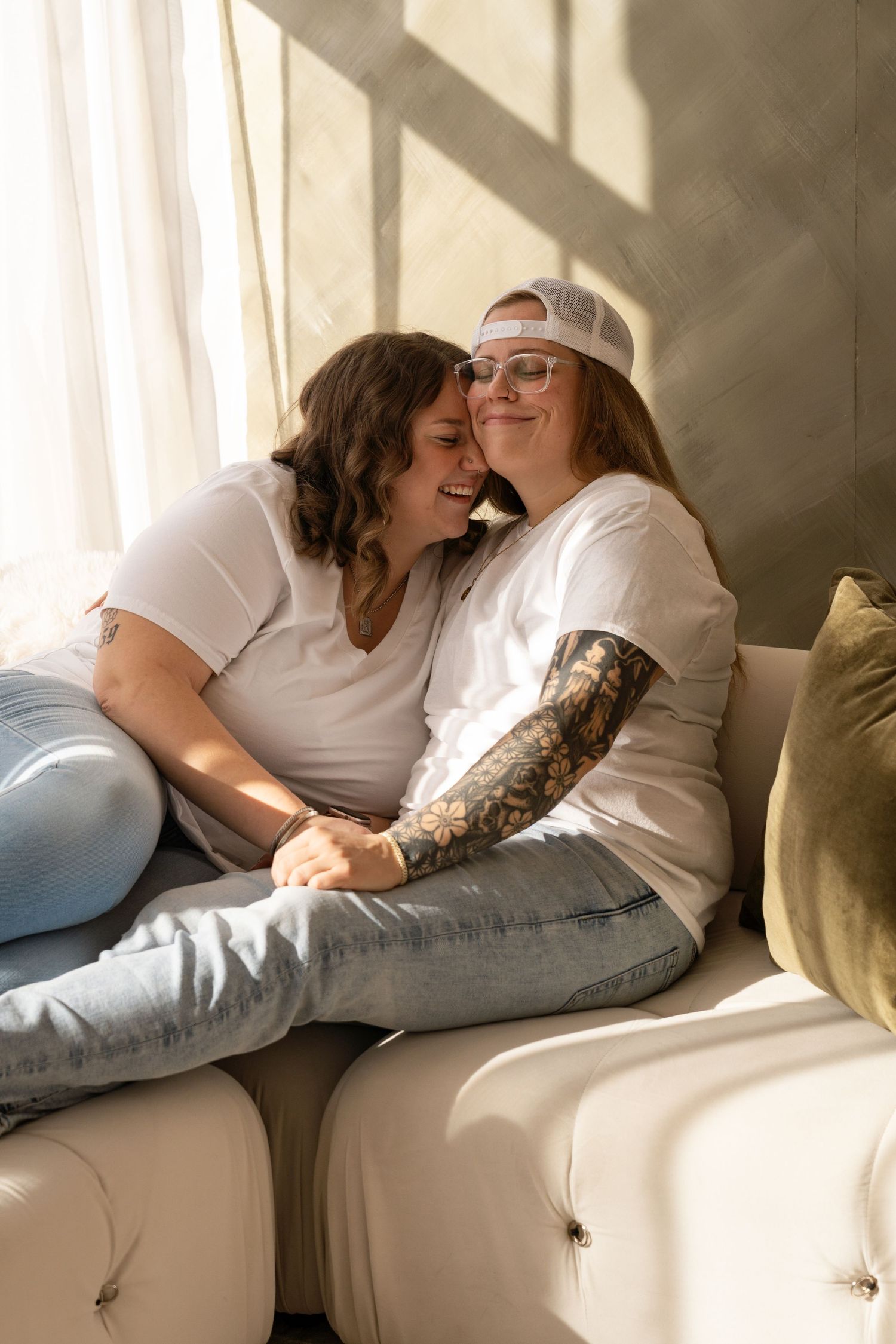 Couple lounging together on white couch in casual attire with natural window light.