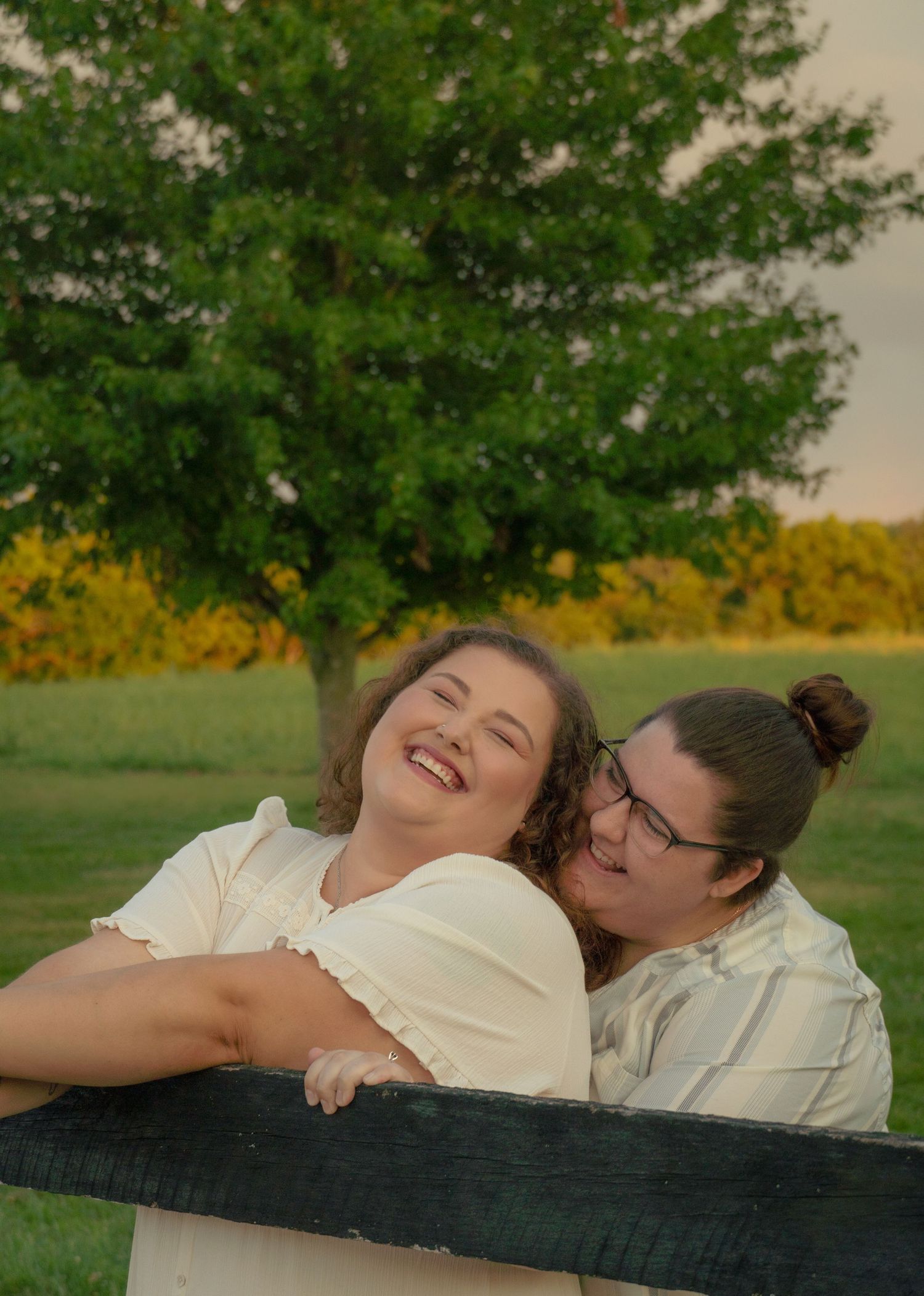 Playful couple laughing together while lying on fence in countryside setting.