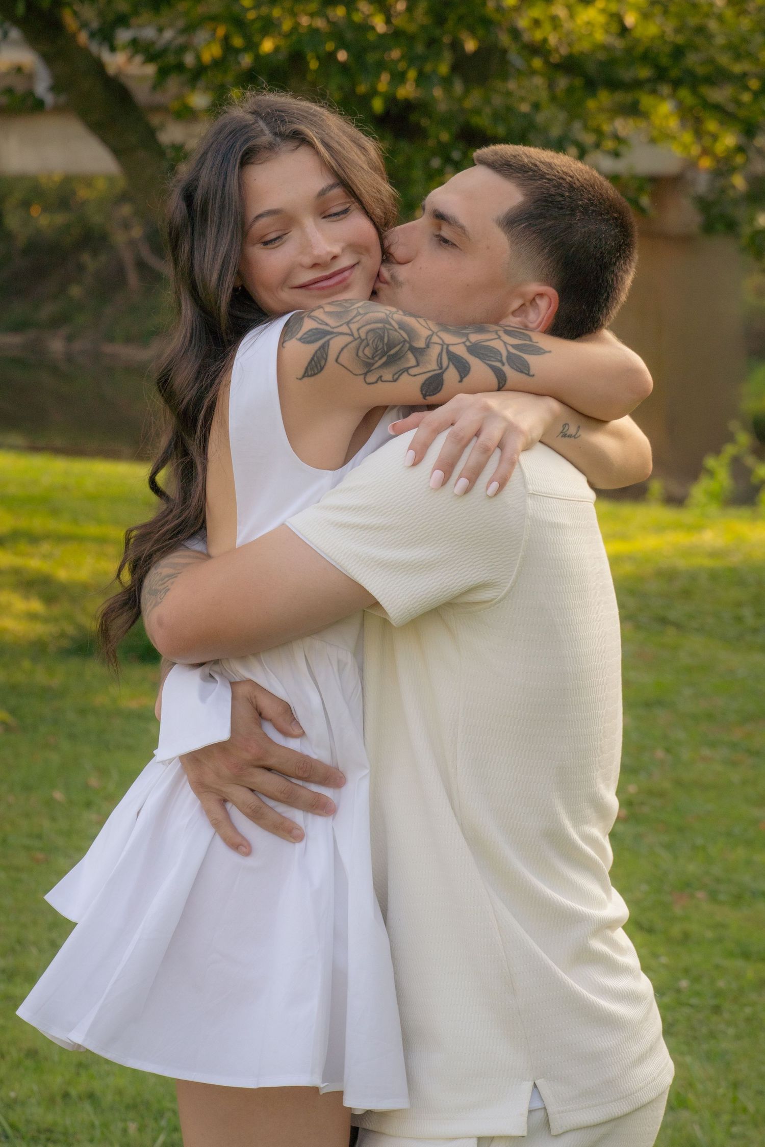 A couple shares intimate moments in a park with golden sunlight filtering through trees.