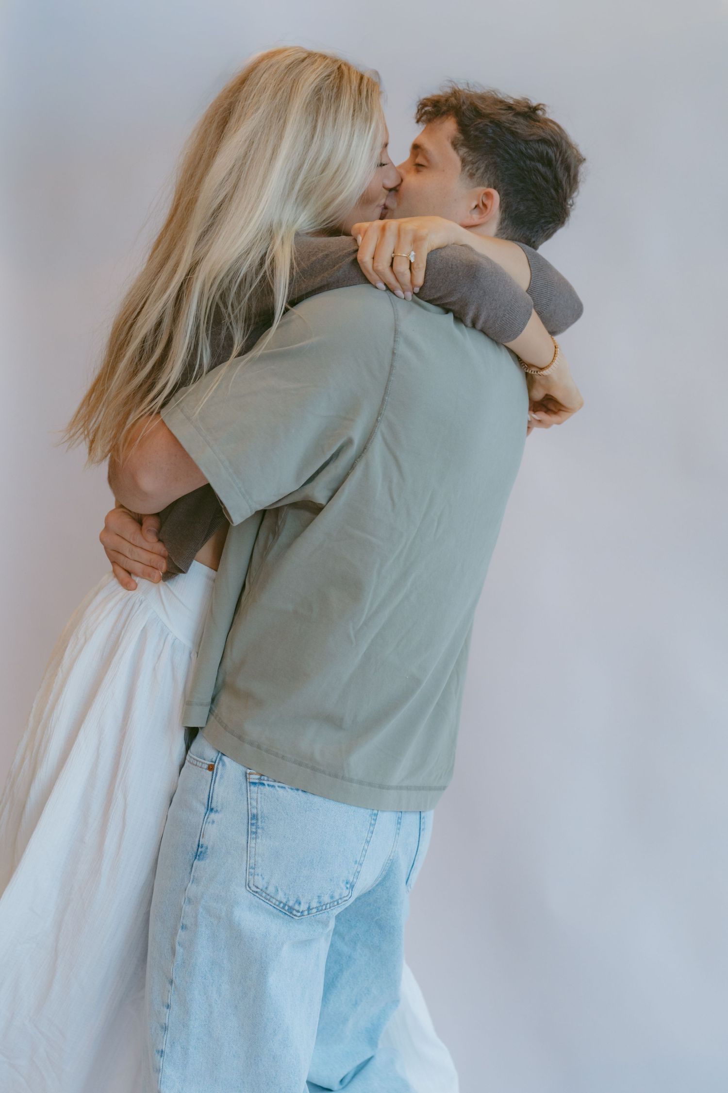 A couple shares an intimate moment against a plain white background, wearing casual clothing.