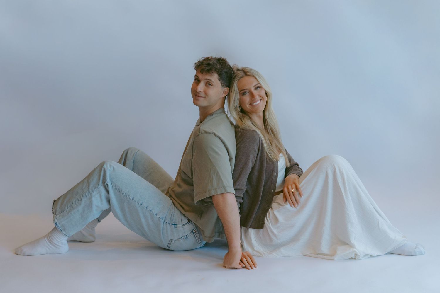 Couple in casual attire poses intimately against light blue background in artistic photoshoot.