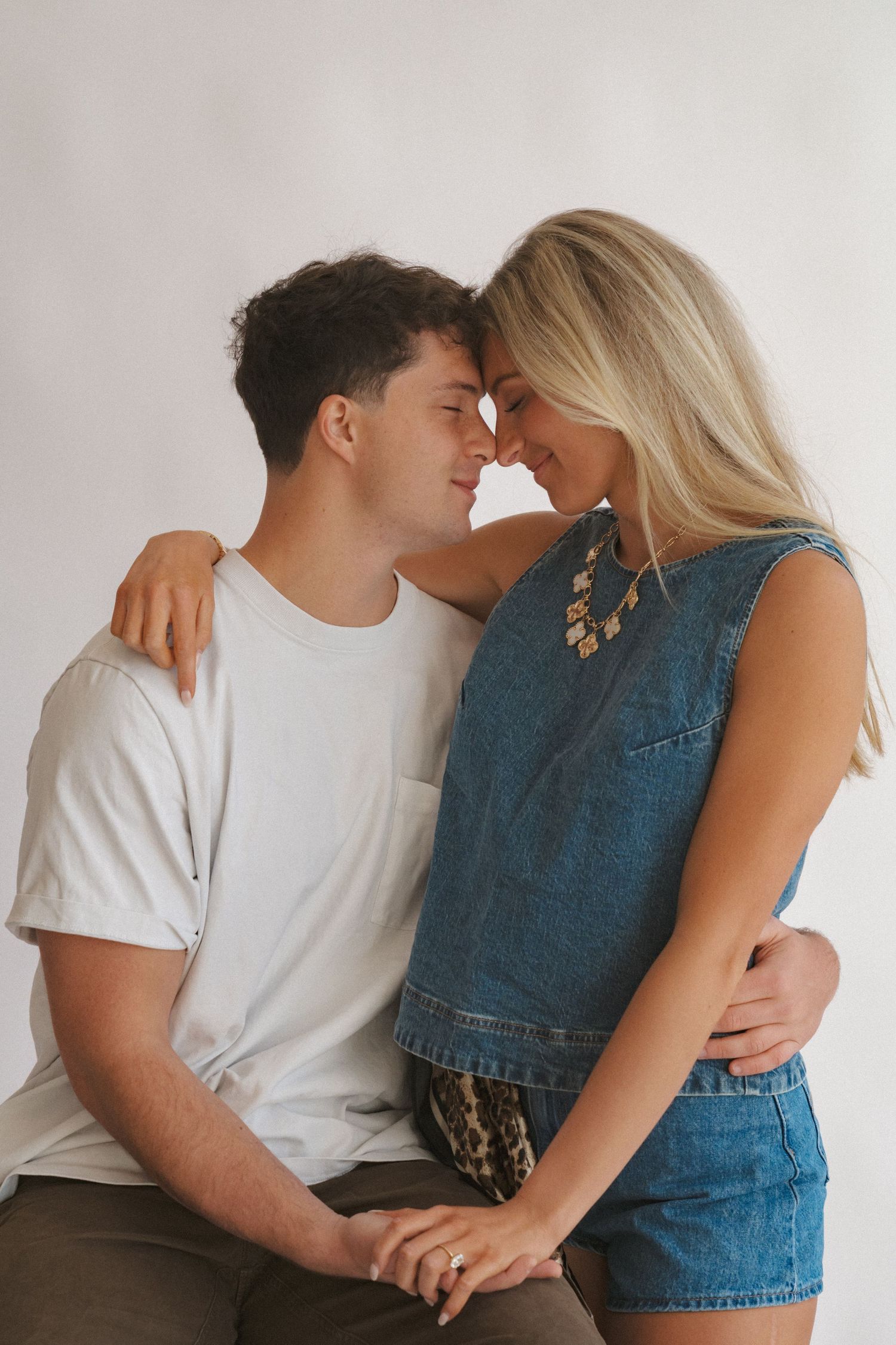 A couple in casual wear shares intimate moments against a white backdrop.
