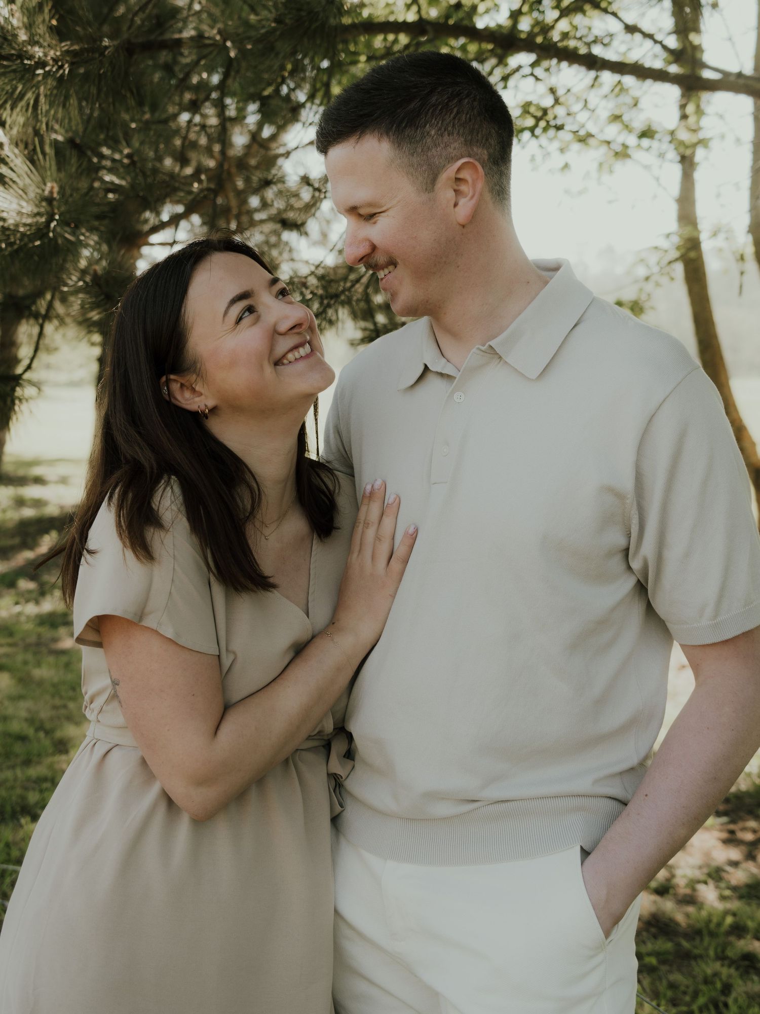 Happy couple sharing a joyful moment outdoors in matching beige outfits among trees.