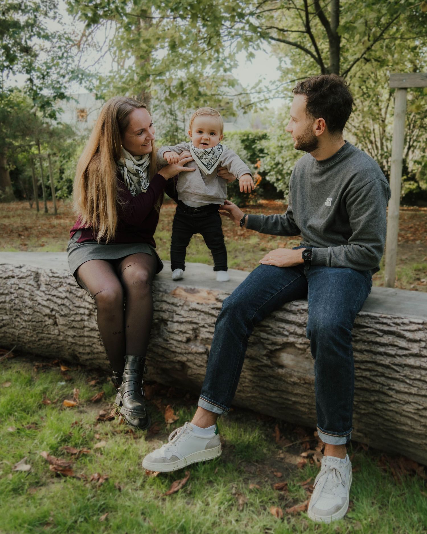 Young family with baby sitting on fallen log in autumn park setting.