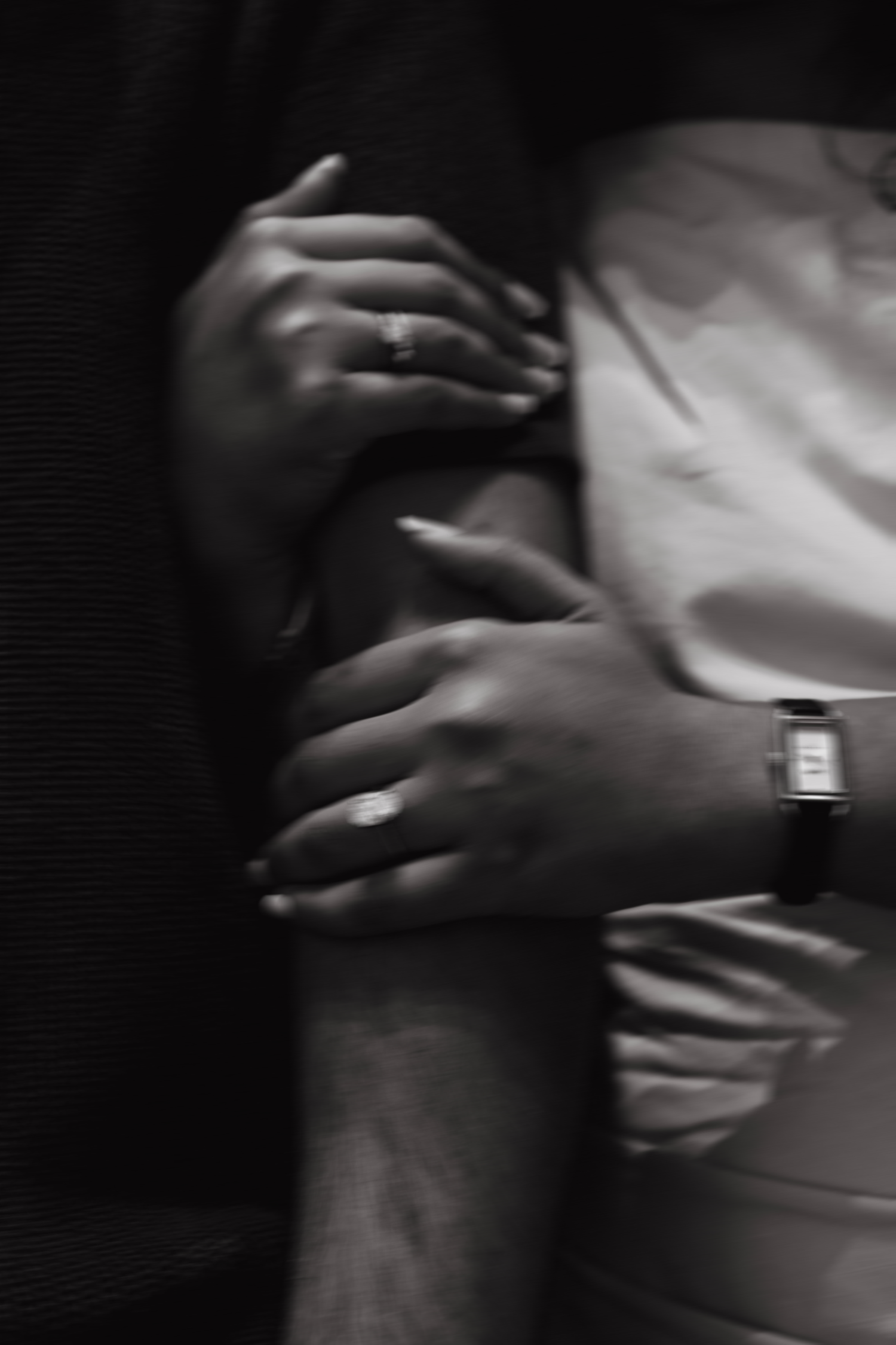 Black and white close-up of a couple holding hands, showing engagement ring and watch details.