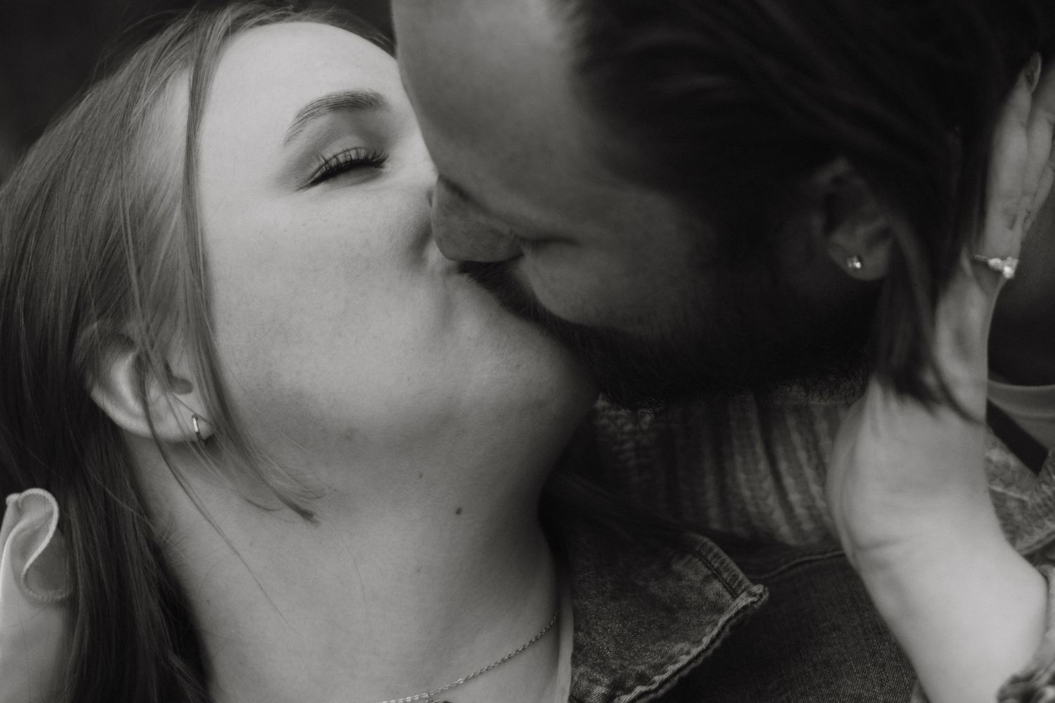 Black and white photo of a couple sharing a romantic kiss in a close-up portrait shot.