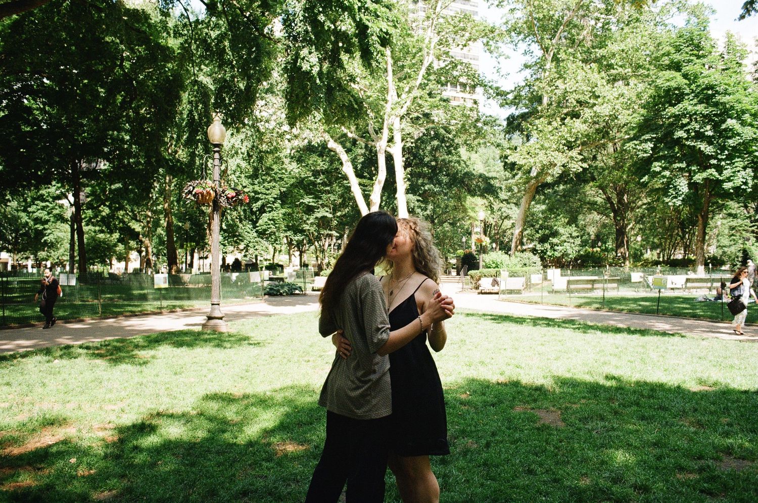 Two young women embracing and dancing together in a lush green park on a sunny day.