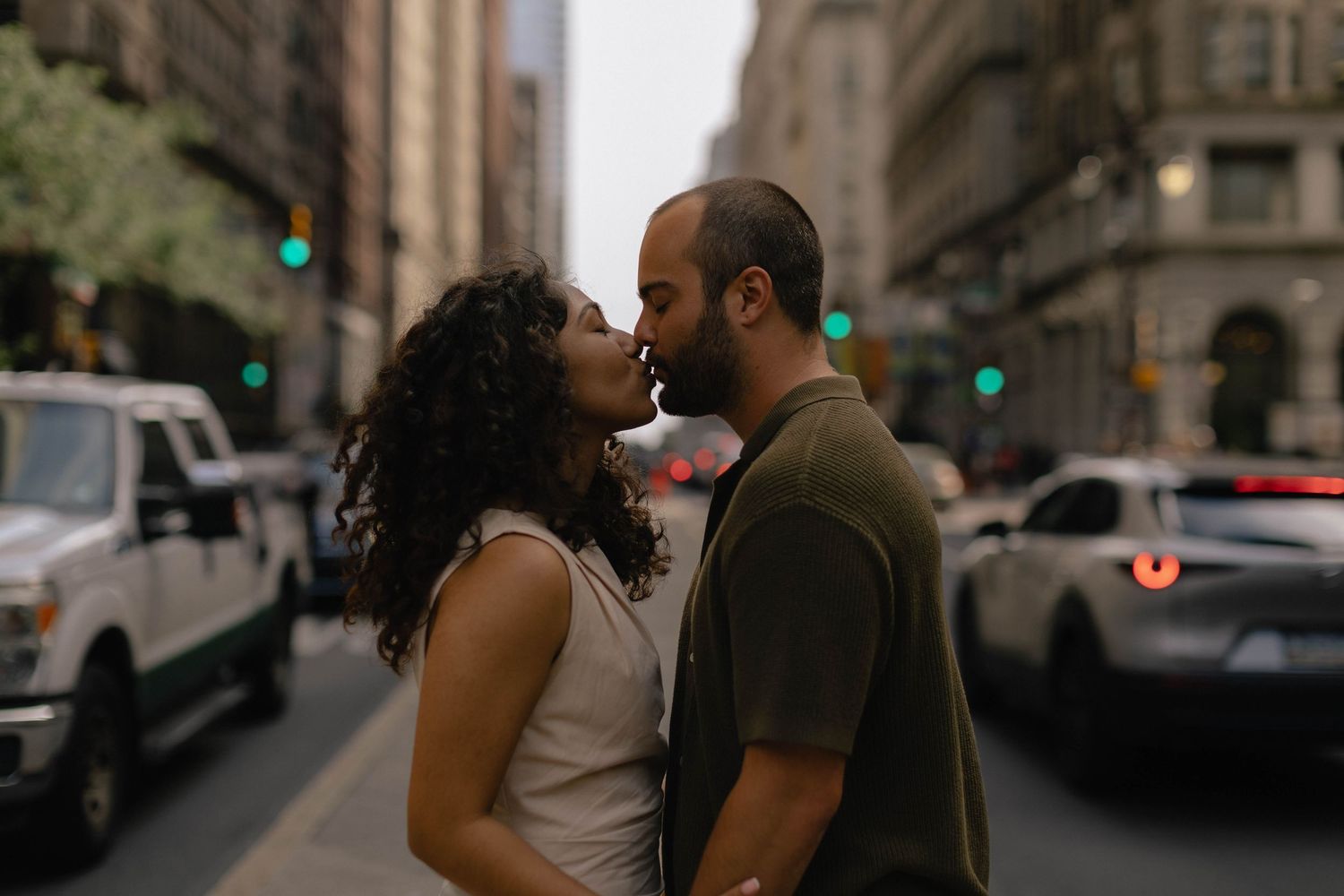 Couple sharing a romantic kiss on a busy urban street surrounded by city traffic and tall buildings.