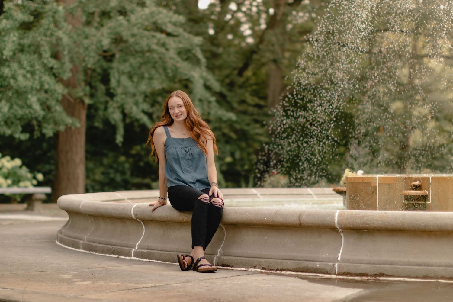 A person in casual attire sits on stone steps outdoors surrounded by lush green trees and foliage.