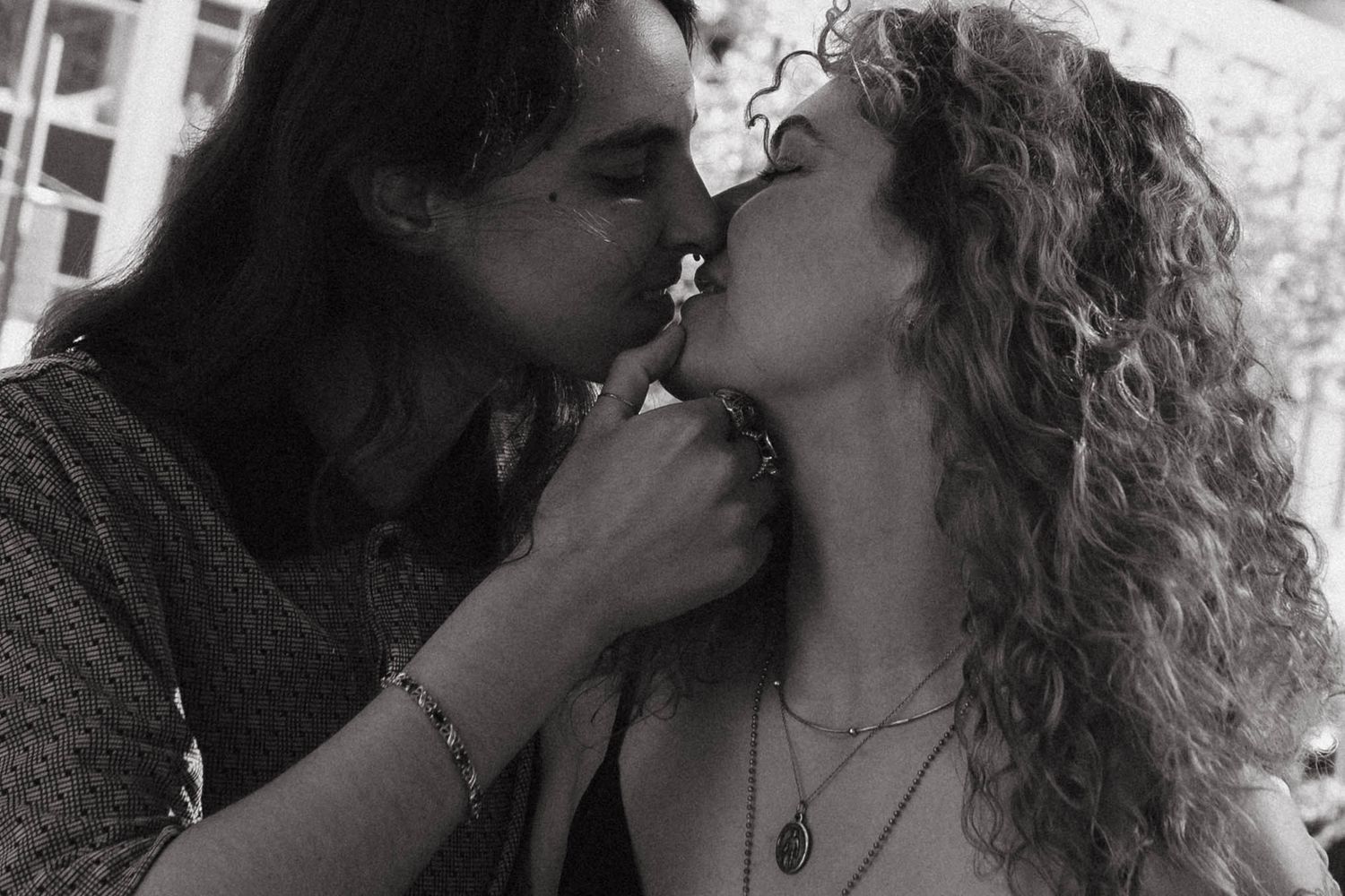 Black and white photo of a couple sharing a romantic kiss, woman with curly hair wearing a necklace.