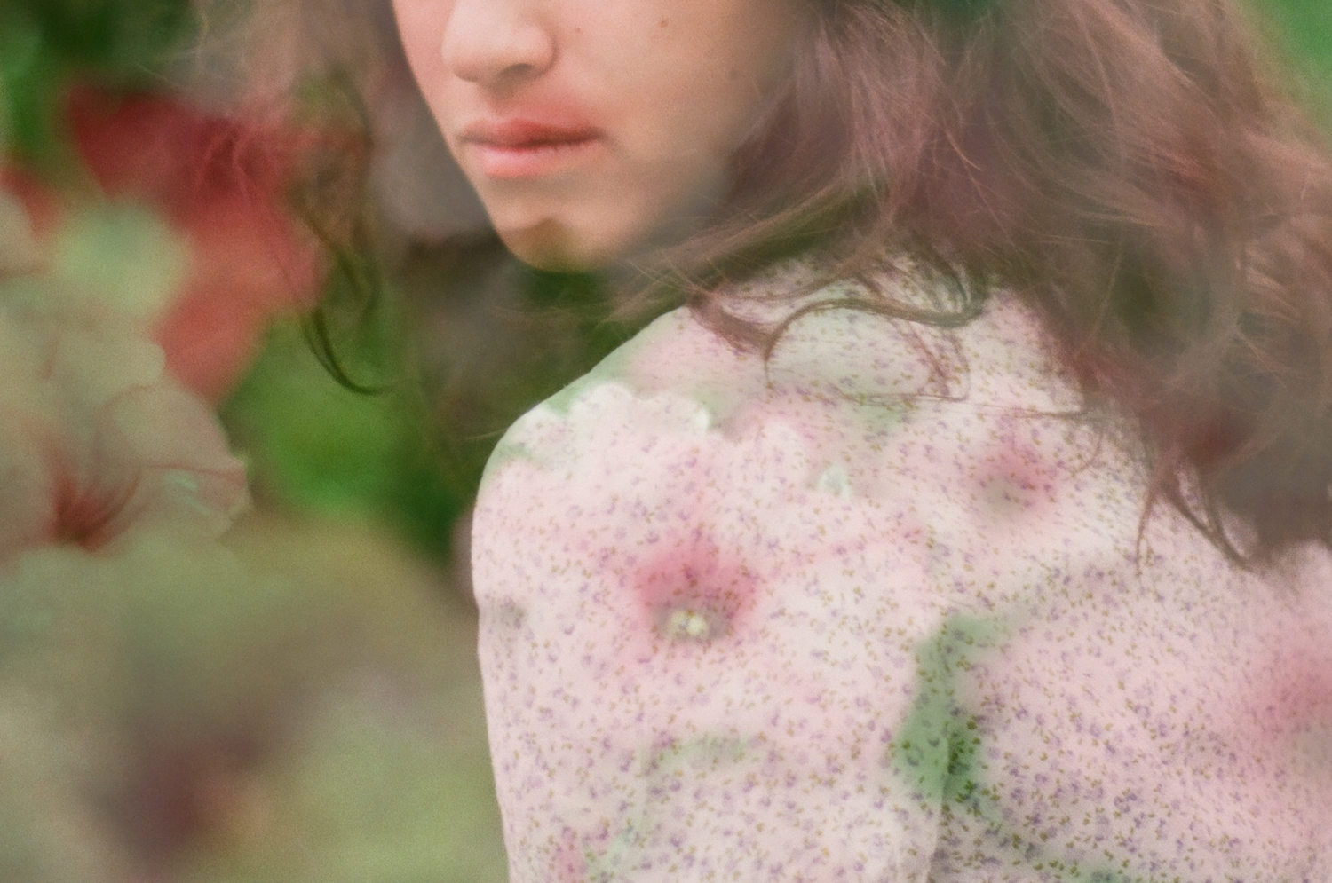 Young woman with flowing hair surrounded by soft pink floral double exposure photography in dreamy garden setting.