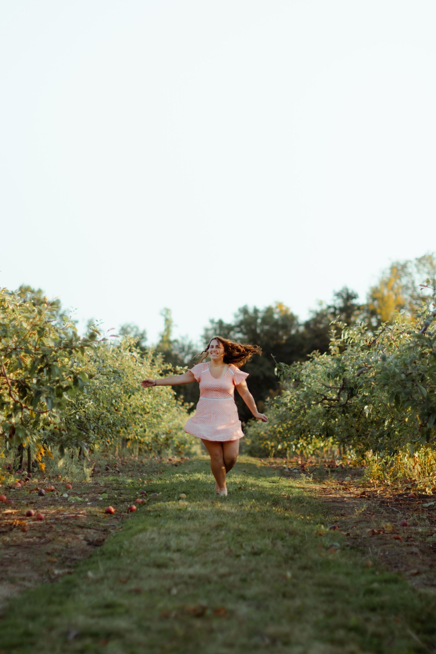 A person in light clothing walks through an orchard during golden hour sunlight.