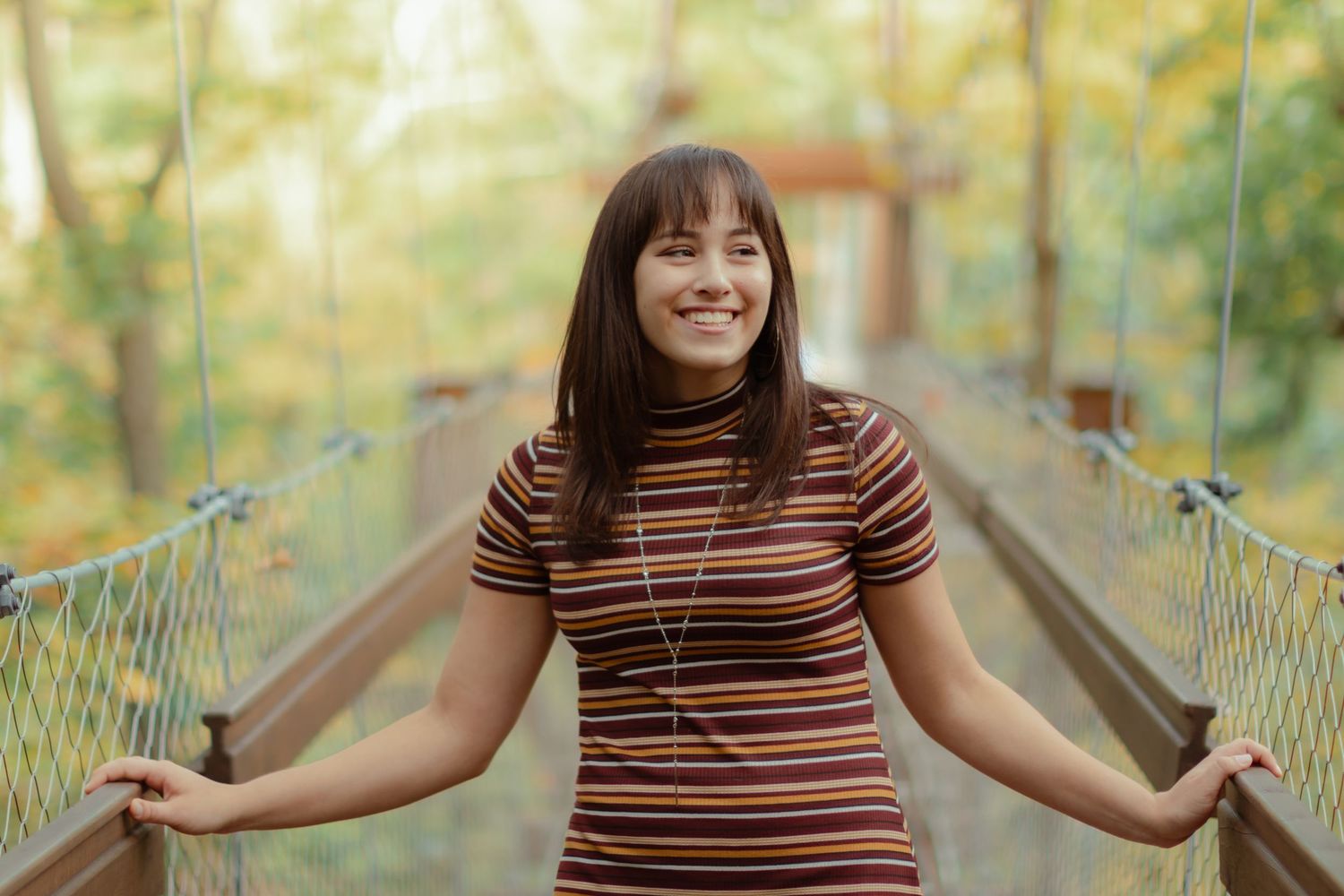 Person in striped shirt posing playfully on a wooden bridge in a park setting.