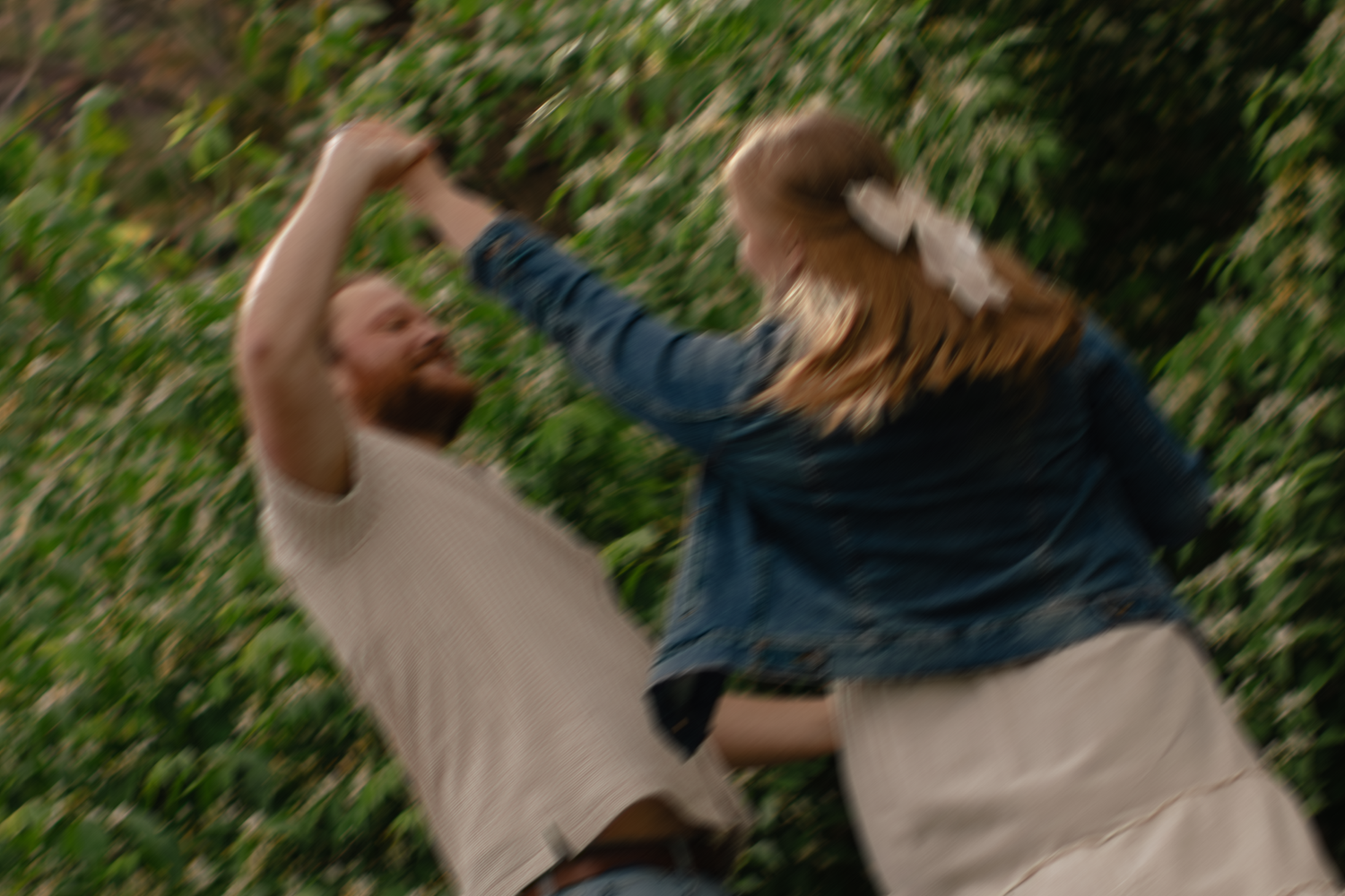 Two people dancing outdoors near lush green foliage, captured in motion blur.