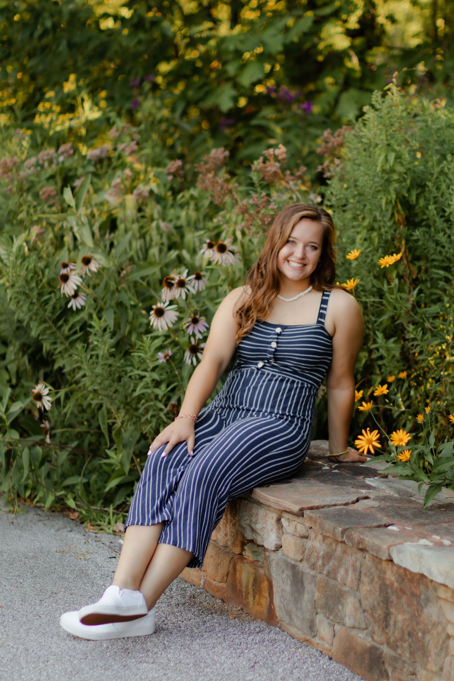A person in a striped dress sitting on a stone wall surrounded by colorful wildflowers.