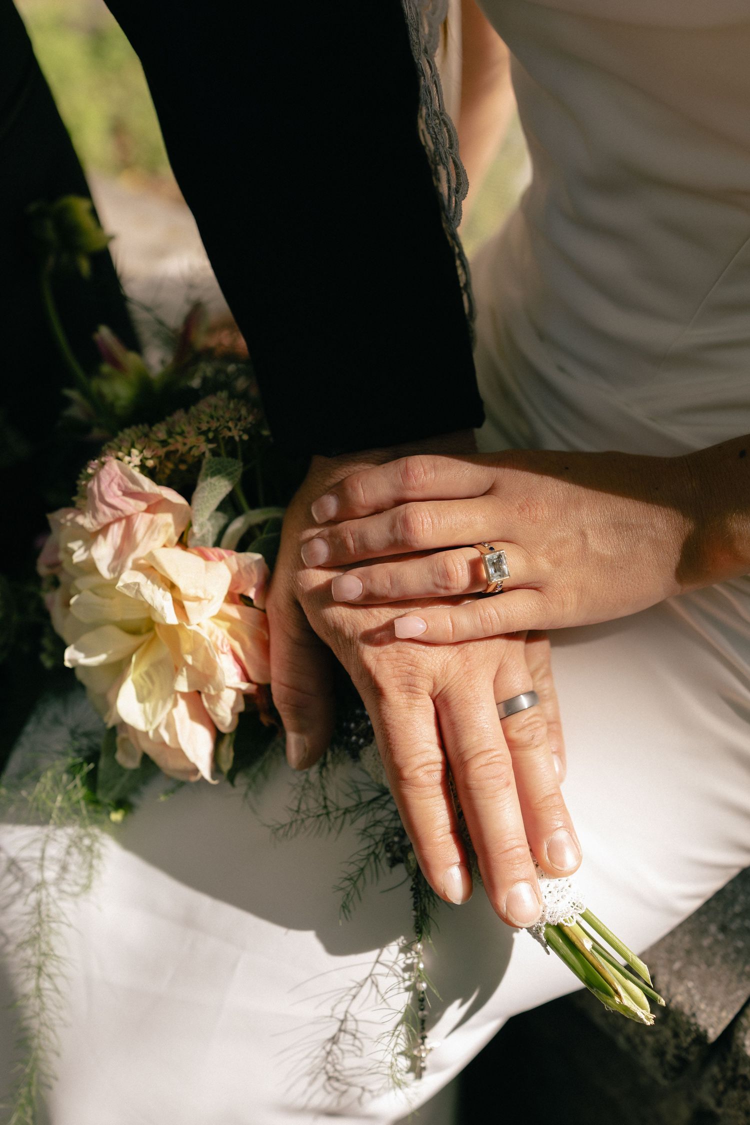 Newlywed couple displaying wedding rings while holding a bridal bouquet of pink and white flowers.