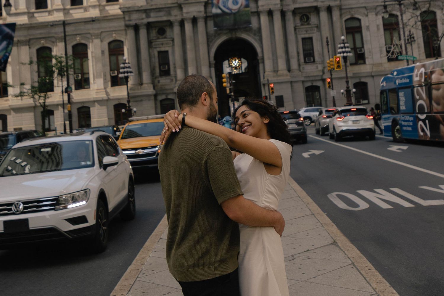 Couple embracing and laughing on a busy city street with classic architecture in the background.