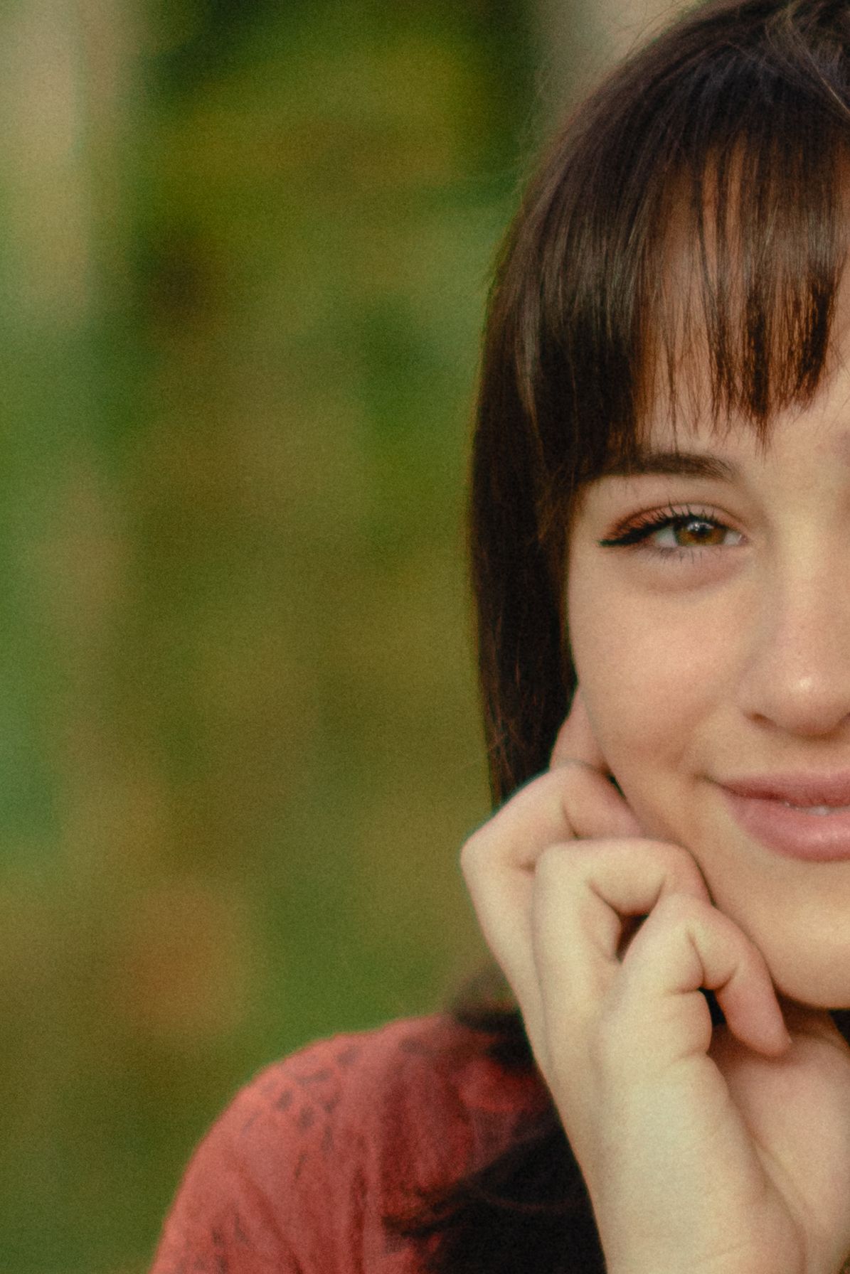 Close-up portrait with a gentle smile and hand resting on cheek against a soft green blurred background.