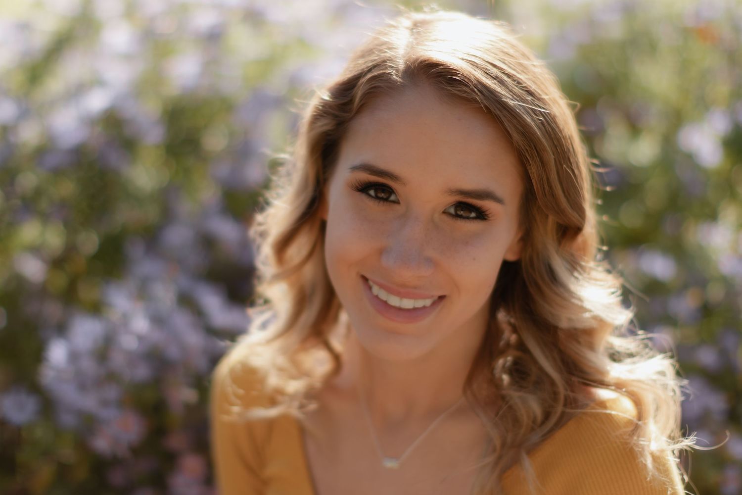 Portrait in yellow top against blurred purple flowers in natural outdoor lighting.