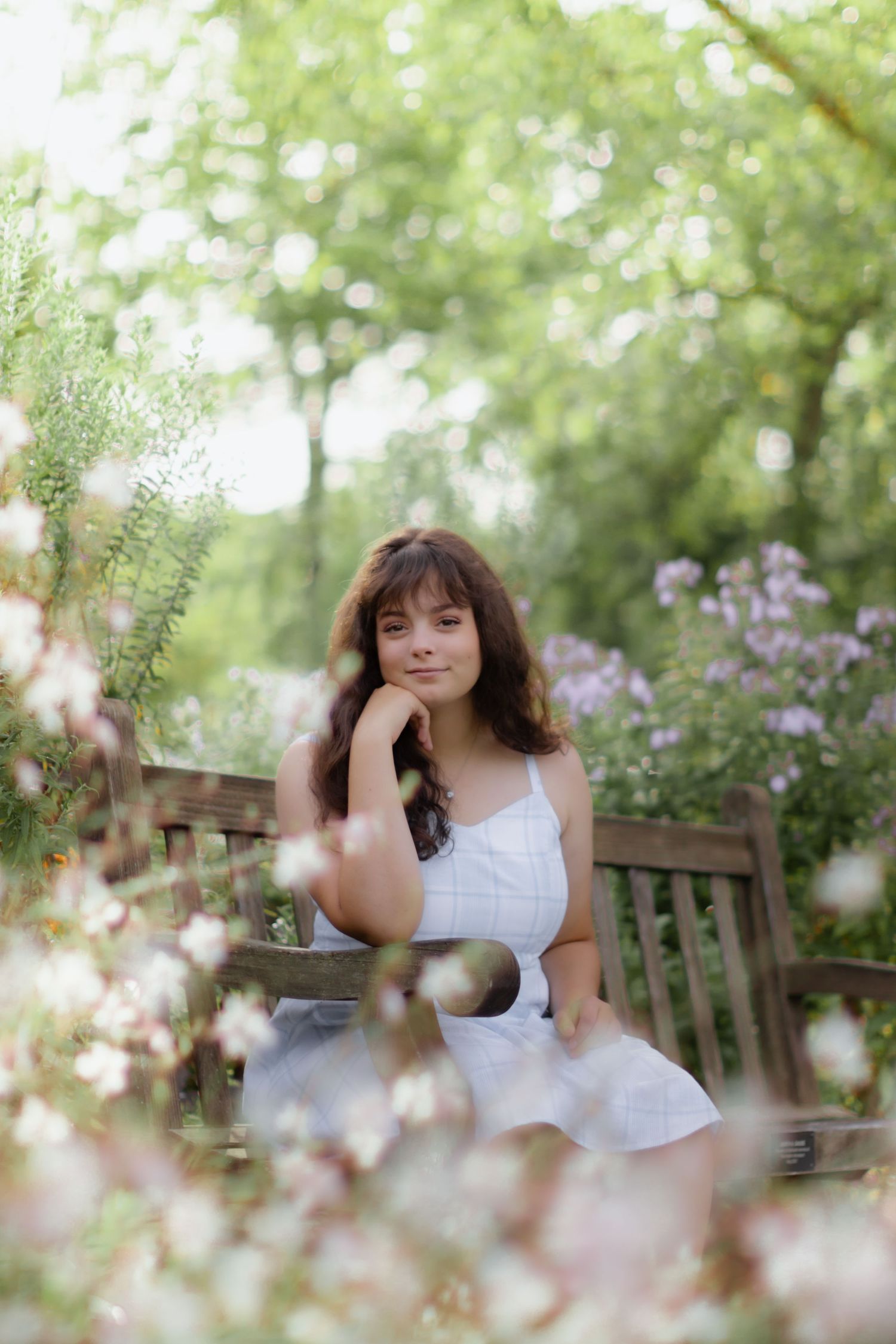 Dreamy garden portrait on wooden bench surrounded by flowers.