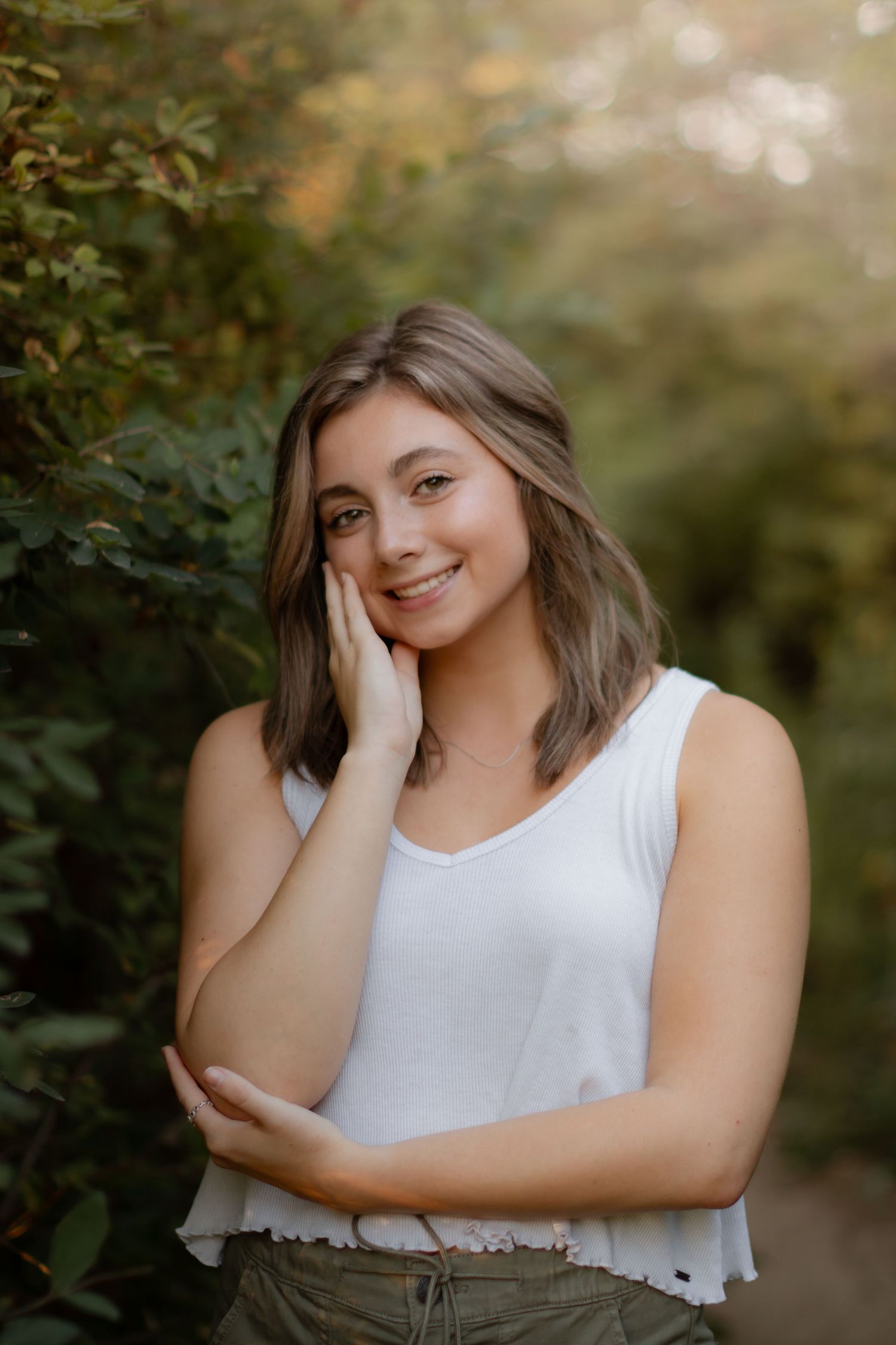 Casual outdoor portrait in white tank top with natural garden backdrop.