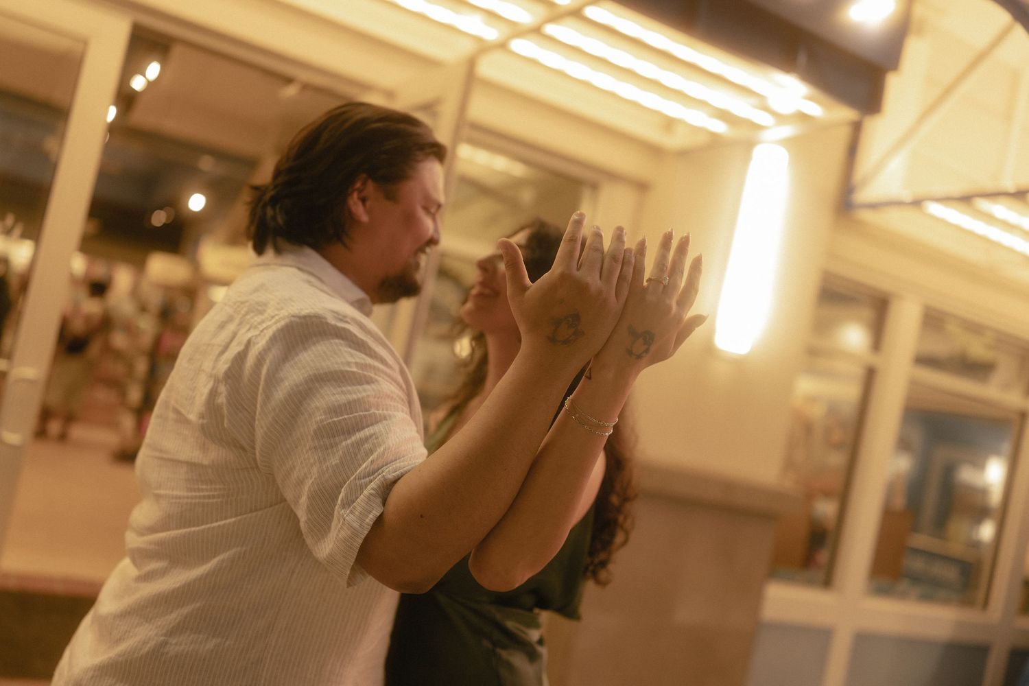 Couple dancing tango in warmly lit venue, man in white shirt leading woman in elegant close embrace.