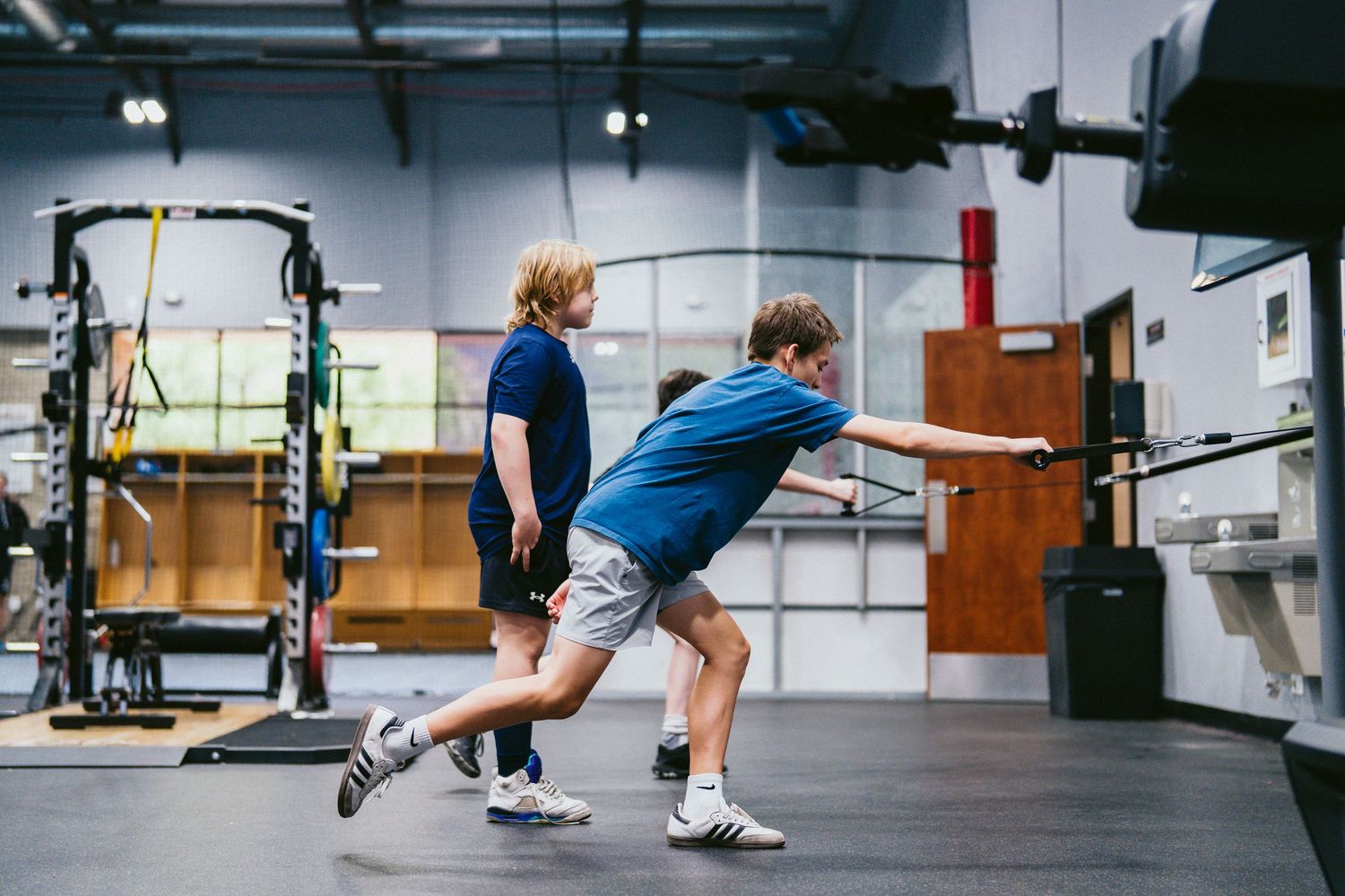 Two young athletes training together in a modern gym, performing resistance band exercises on turf.