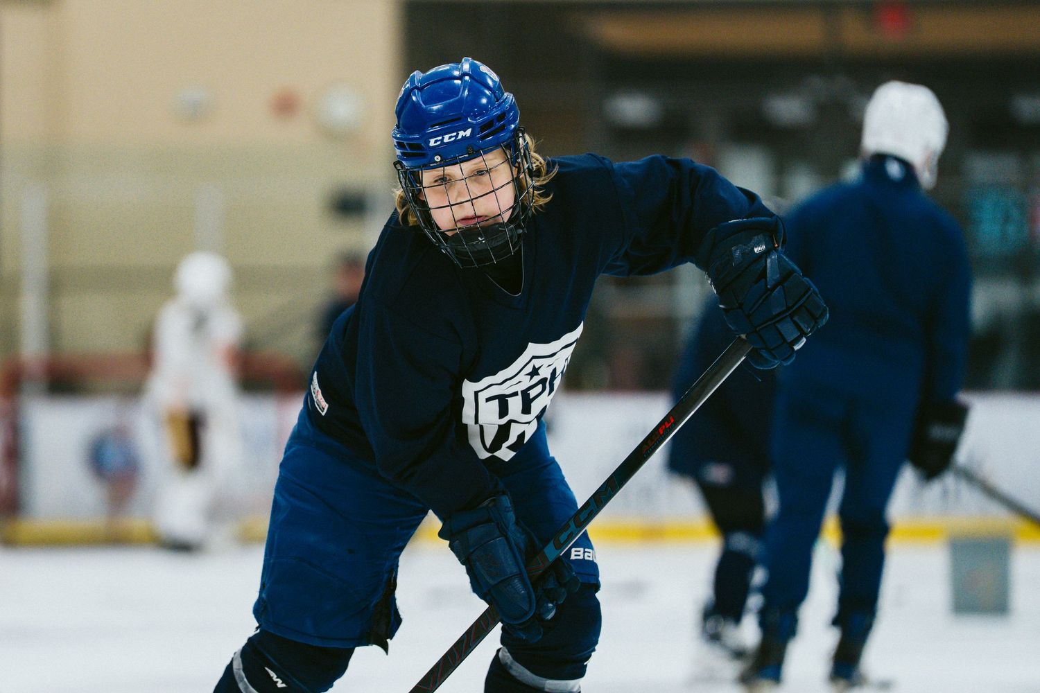 Female hockey player in blue jersey and helmet skating with stick during ice hockey practice.