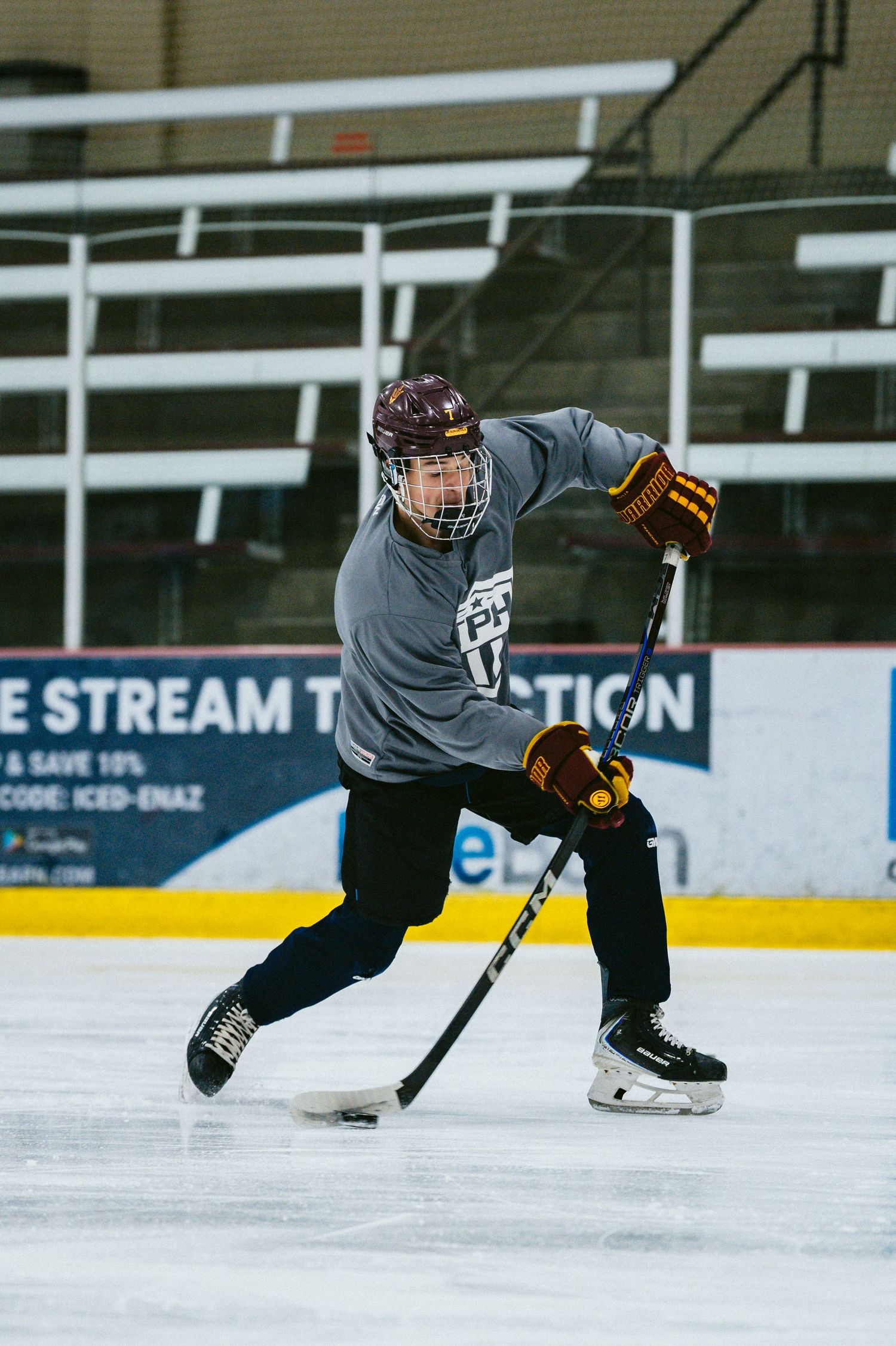 Hockey player in gray jersey and maroon helmet executes sharp turn while controlling puck on ice.