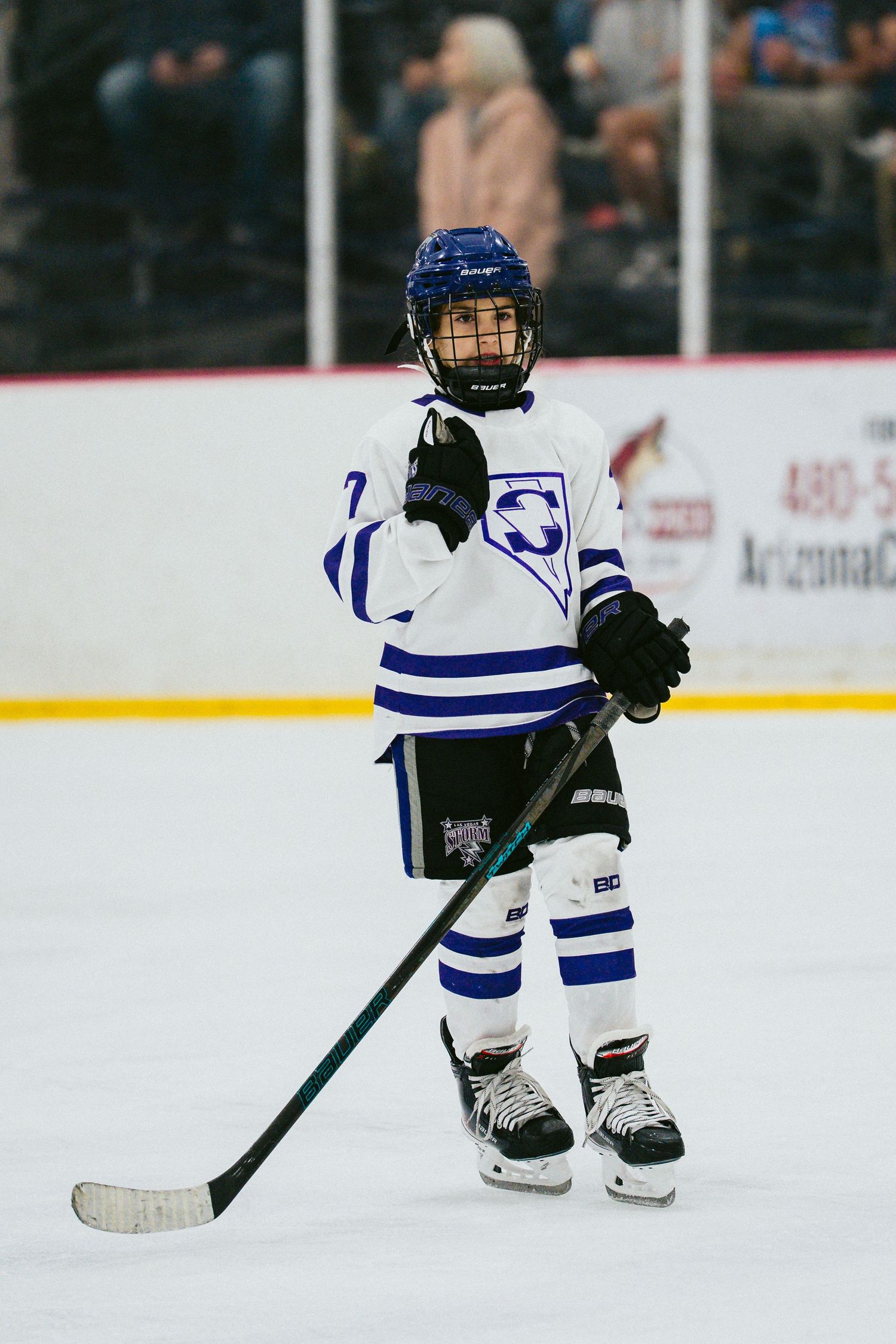 Youth hockey player in blue and white uniform stands ready with stick on ice.