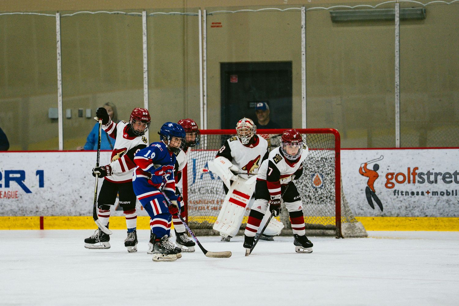 Youth hockey players compete for the puck during an intense game at an indoor ice rink.
