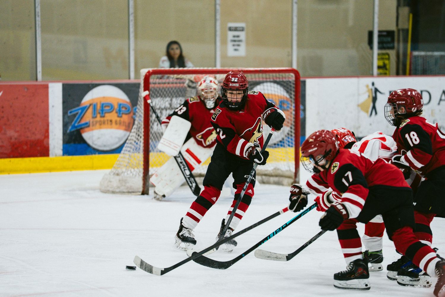 Youth hockey players in red uniforms practice drills on the rink.