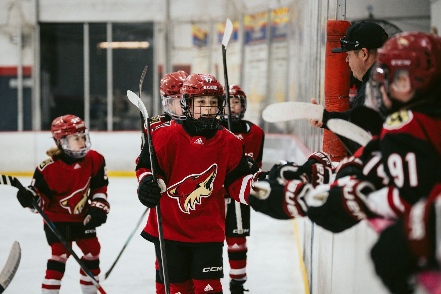 Youth hockey players in red jerseys move across the ice during a game.