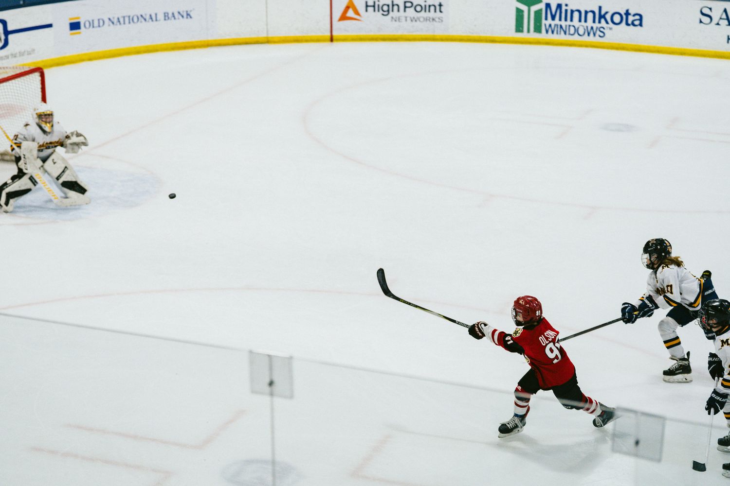 Hockey players competing near goal with advertising banners visible above rink.