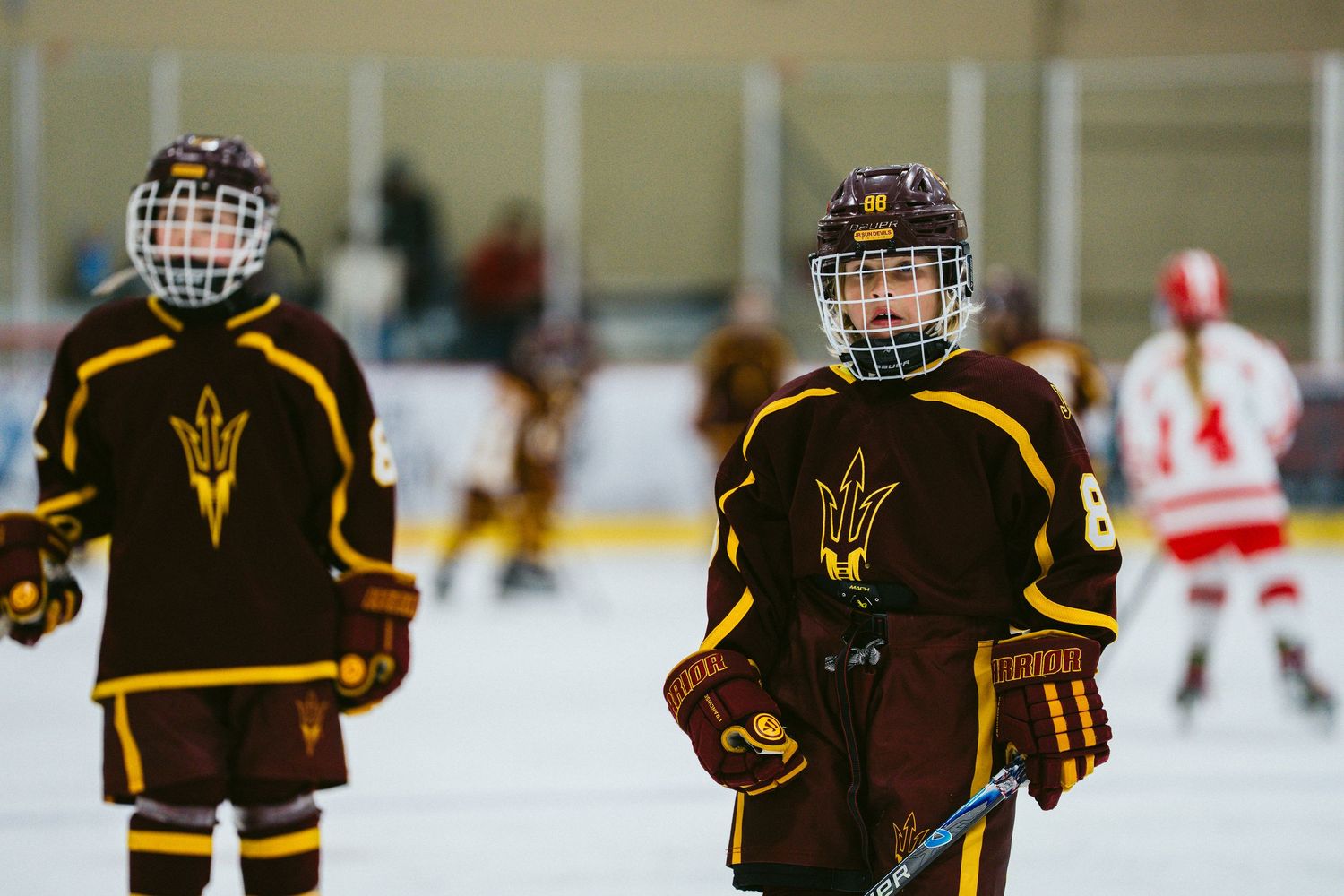 Youth hockey players in brown and gold jerseys line up on the ice during a game.