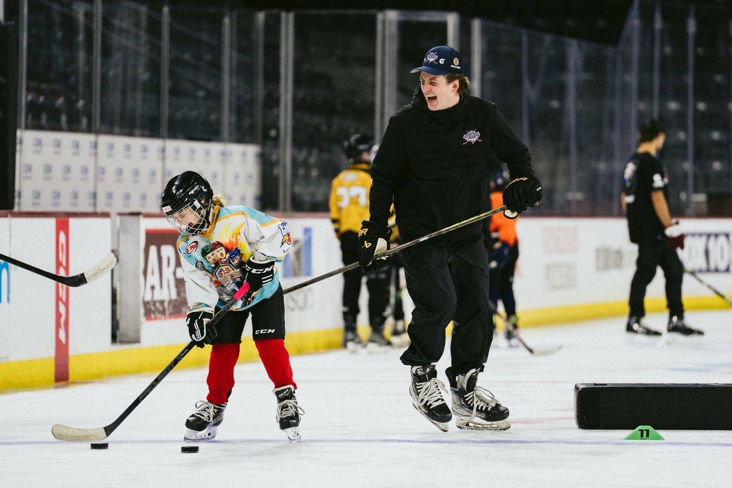 Hockey coach instructs young player on puck handling technique during youth ice hockey practice session.