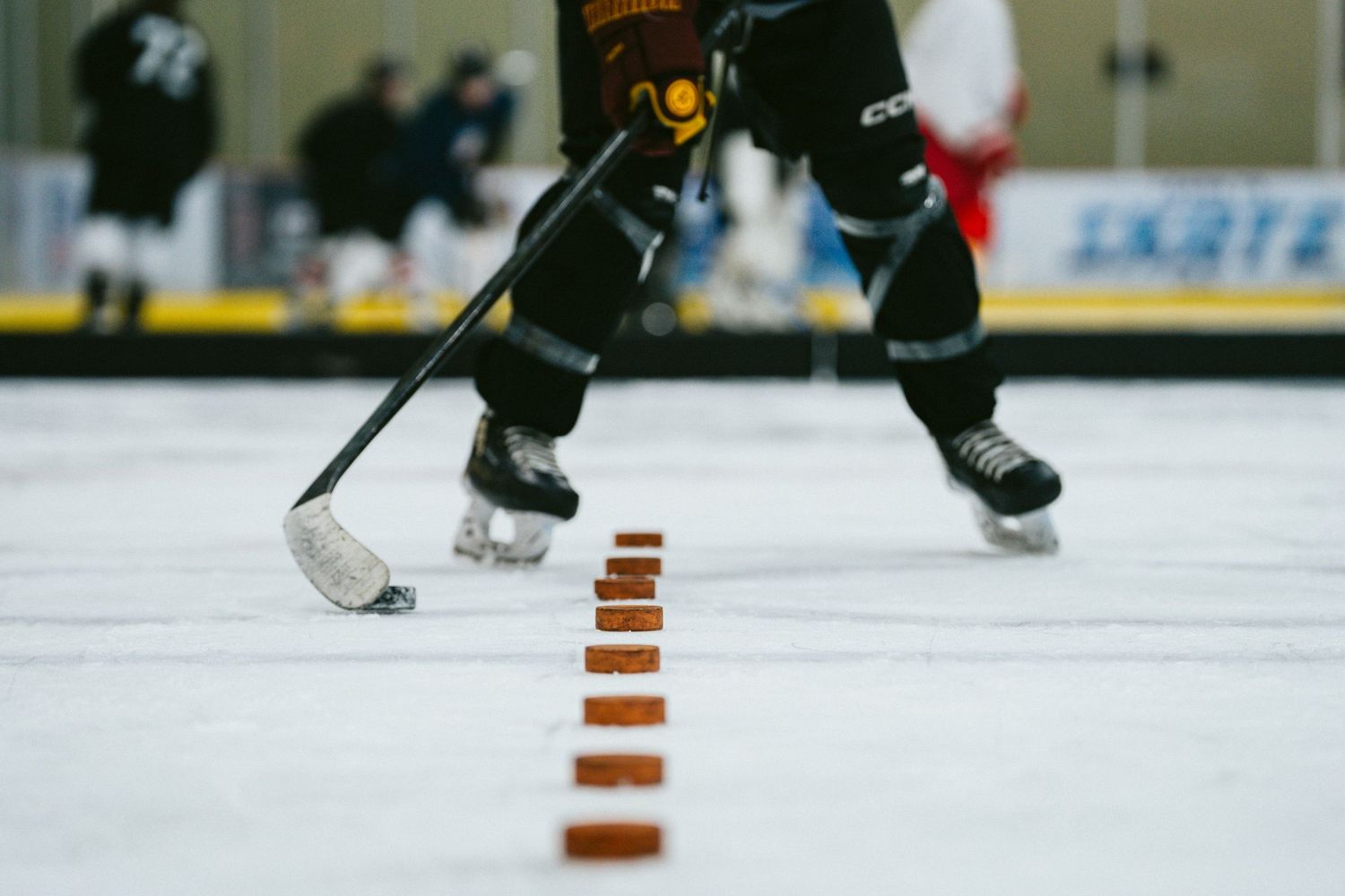 Ice hockey player in black uniform skating past a line of orange pucks during a drill at an indoor ice rink.