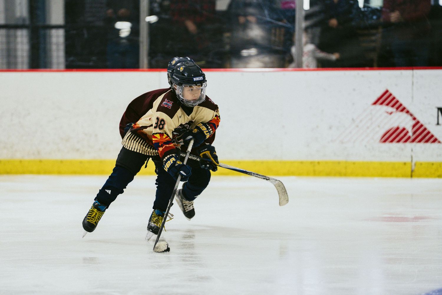 Young hockey player in gold and black jersey skates with the puck during a youth game.