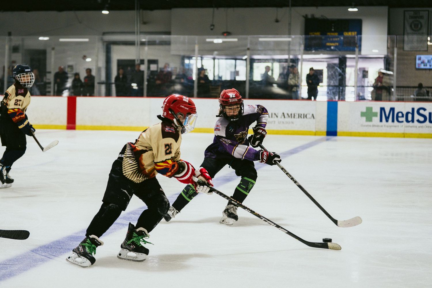 Two young ice hockey players battle for the puck during a competitive youth hockey game on indoor rink.