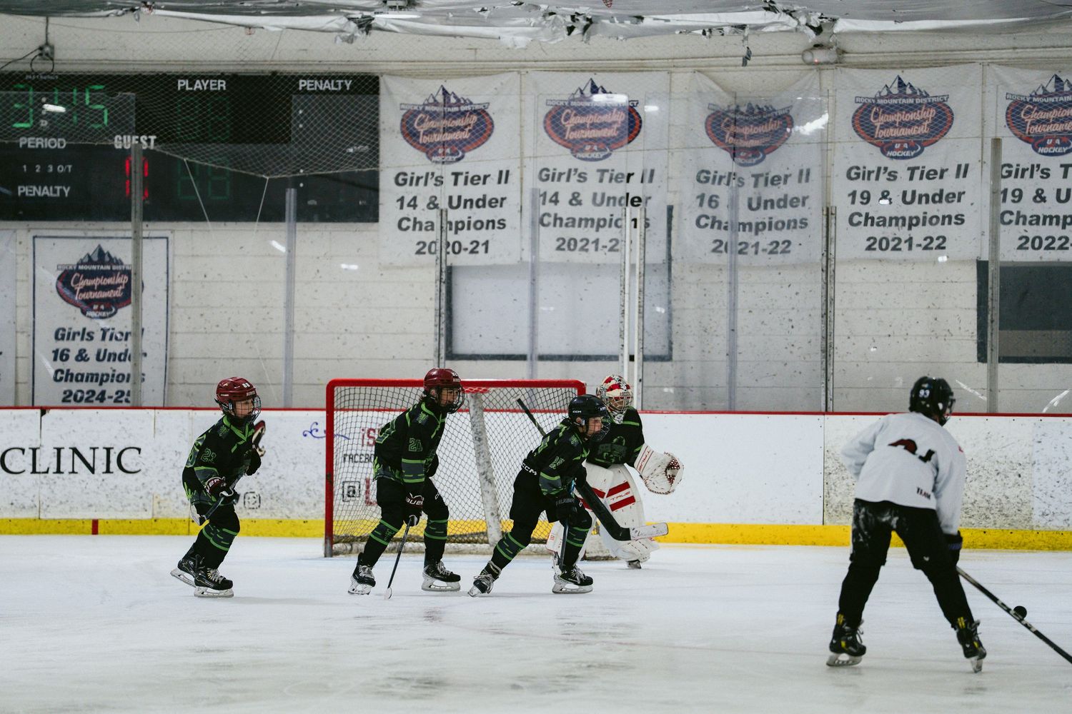 Youth hockey players in green jerseys practicing drills on indoor ice rink with championship banners above.
