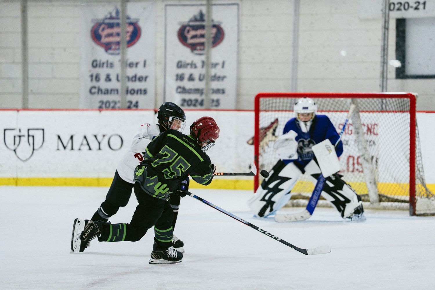 Young hockey player in black uniform takes a shot on goal during a youth ice hockey game.