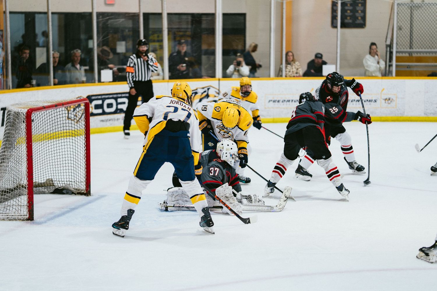 Hockey players in yellow and dark uniforms battle for the puck near the goal during a game.