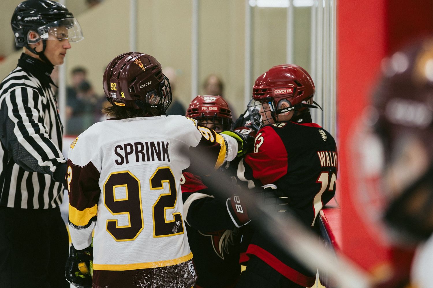 Hockey player Sprink #92 in a physical confrontation near the boards during an intense ice hockey game.